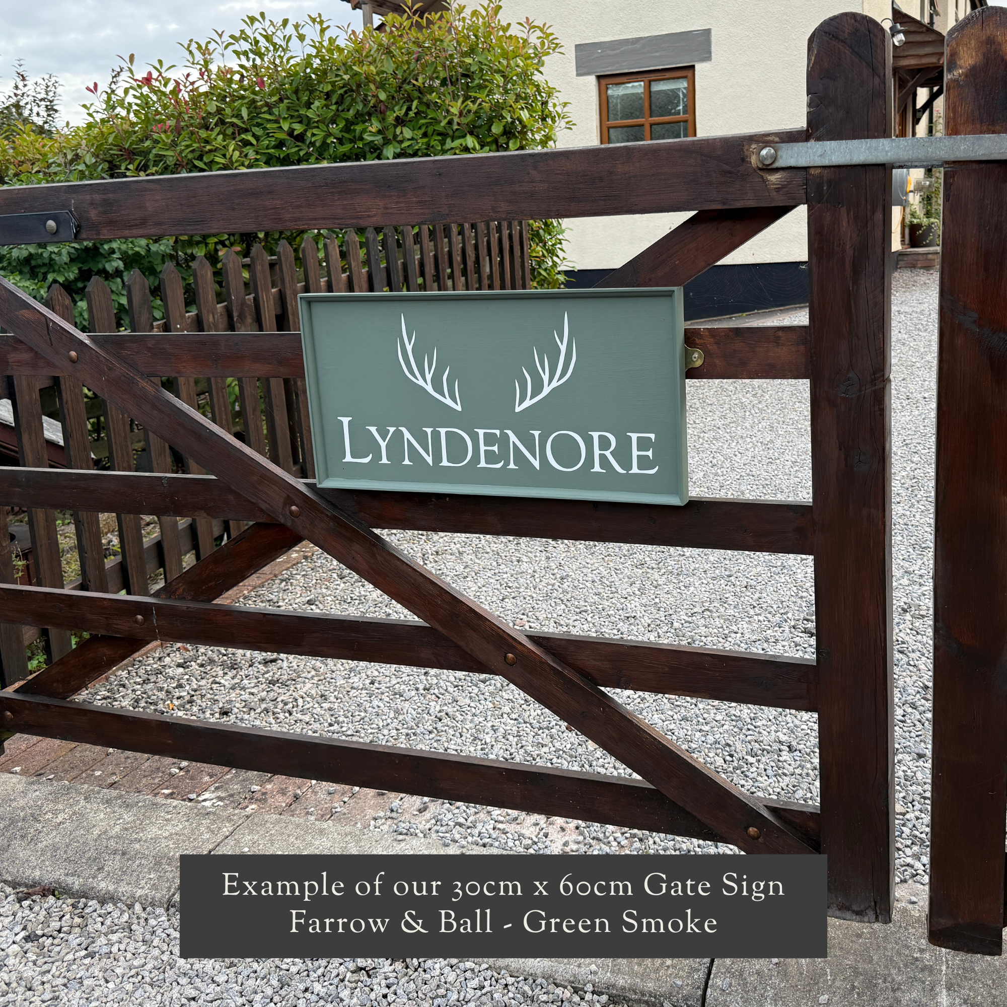 Painted and framed gate sign on a wooden gate with a building and greenery in the background