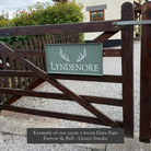 Painted and framed gate sign on a wooden gate with a building and greenery in the background 